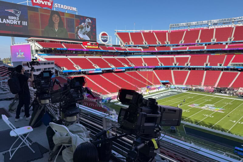 Television broadcast cameras set up in a stadium overlooking a football field, with empty red seats and a large screen displaying a sports broadcast. The stadium scoreboard reads "Levi's Stadium.