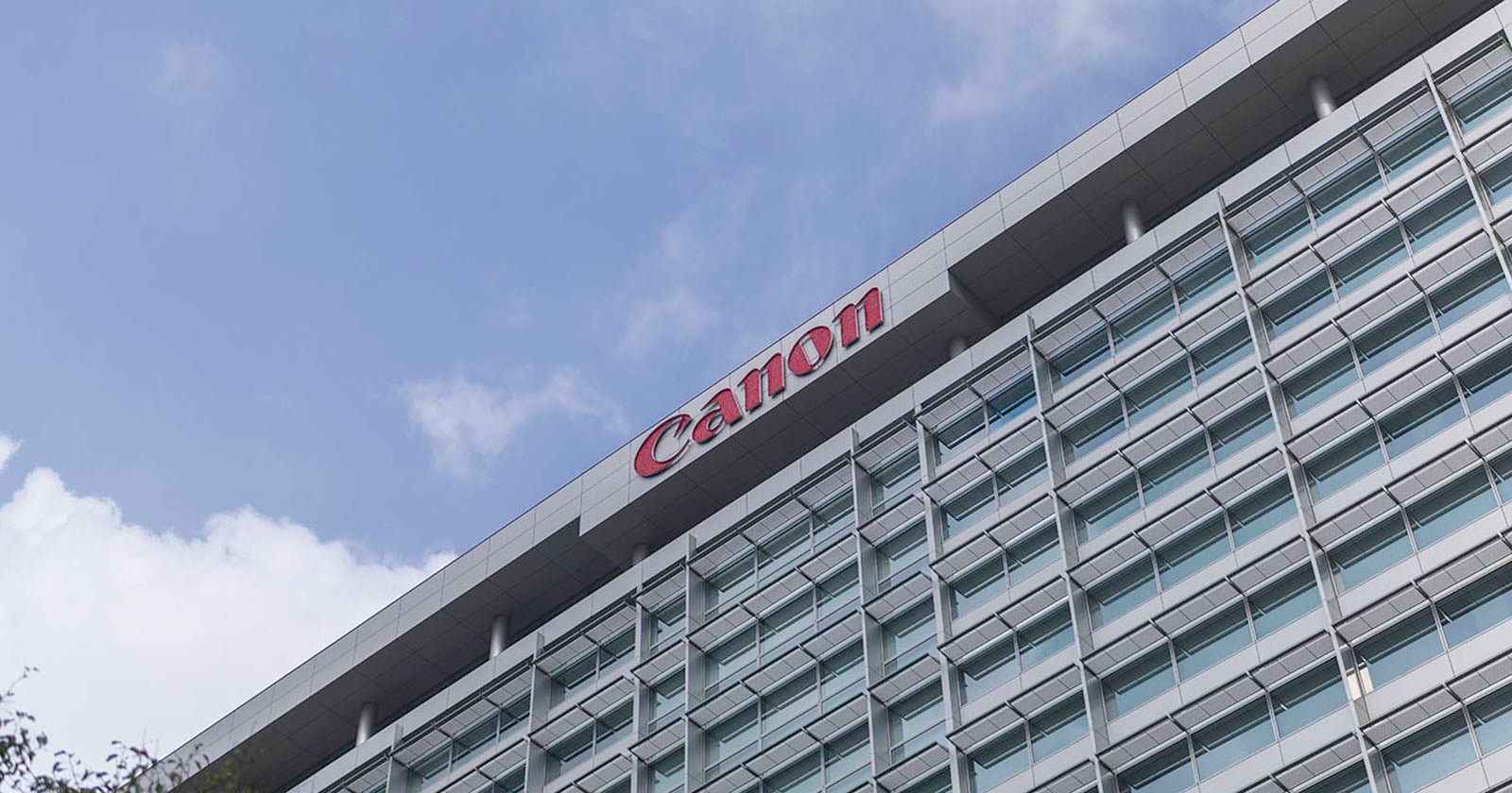A modern glass office building with the red Canon logo on the upper facade, set against a blue sky with some clouds.