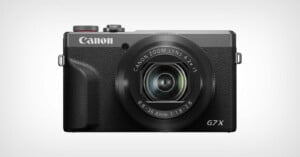 A Canon G7 X digital camera with a black body, prominent zoom lens, and Canon logo on the top left, shown facing forward against a plain light background.