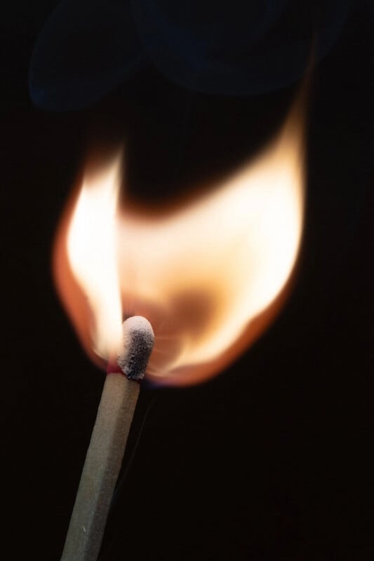 Primer plano de una cerilla encendida con llamas de color naranja y amarillo brillante sobre un fondo negro oscuro. La cabeza de la cerilla era blanca y parcialmente carbonizada.