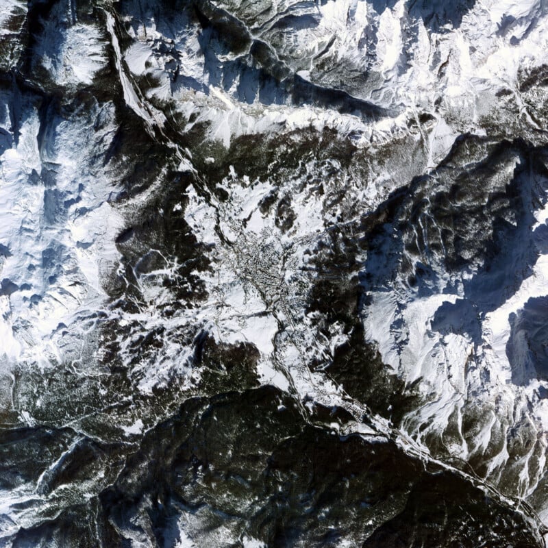 La vista satelital muestra un paisaje montañoso cubierto de nieve con una ciudad en el centro rodeada de un terreno forestal escarpado y picos montañosos. Las carreteras se extienden hacia el exterior y conectan la ciudad con las zonas circundantes.