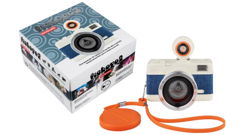 A white and blue instant film camera with an orange wrist strap is next to its packaging box, which displays images and branding for the "Fisheye No. 2" camera and includes sample photos.