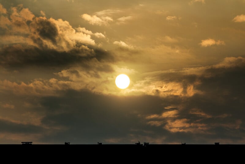 La luz del sol brilla a través de espectaculares nubes doradas sobre el techo oscuro y cincelado, con pequeñas estructuras visibles a lo largo de los bordes.