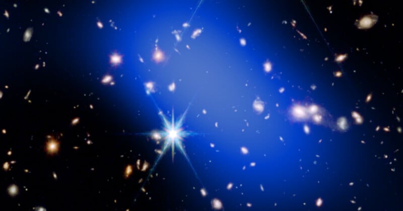 An image of deep space shows numerous distant galaxies and stars on a dark background. A bright blue glow, representing dark matter, surrounds the galaxies, and a star with visible light flares shines in the lower center.