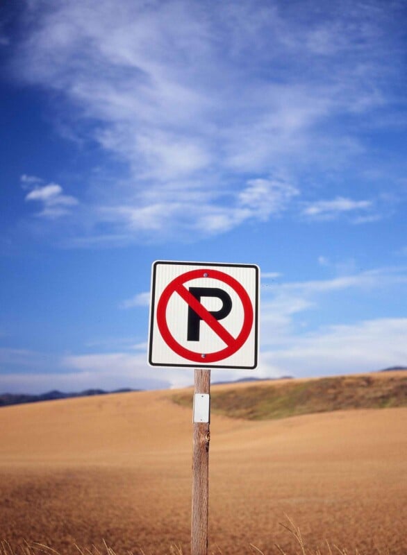 Bajo el cielo azul y las nubes blancas, en un espacio abierto seco y cubierto de hierba, había un cartel de 