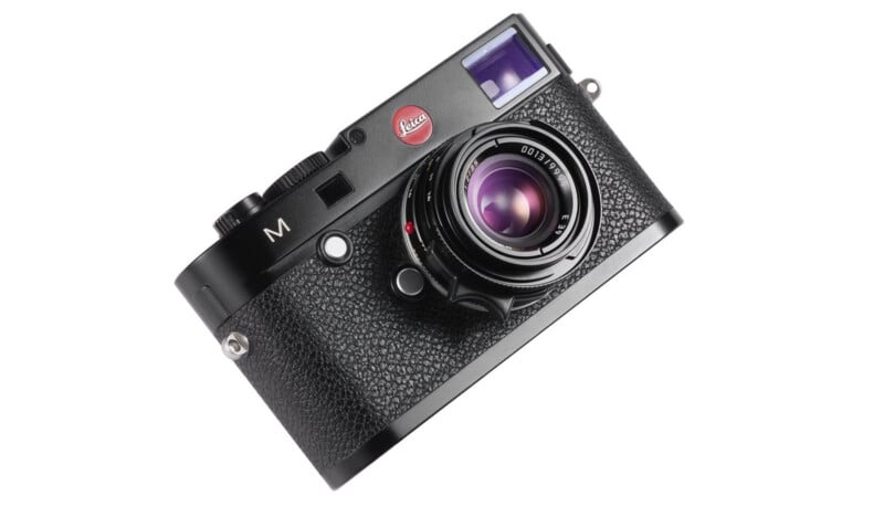 A black Leica M digital rangefinder camera with a textured grip, prominent lens, and red Leica logo, displayed at an angle on a white background.