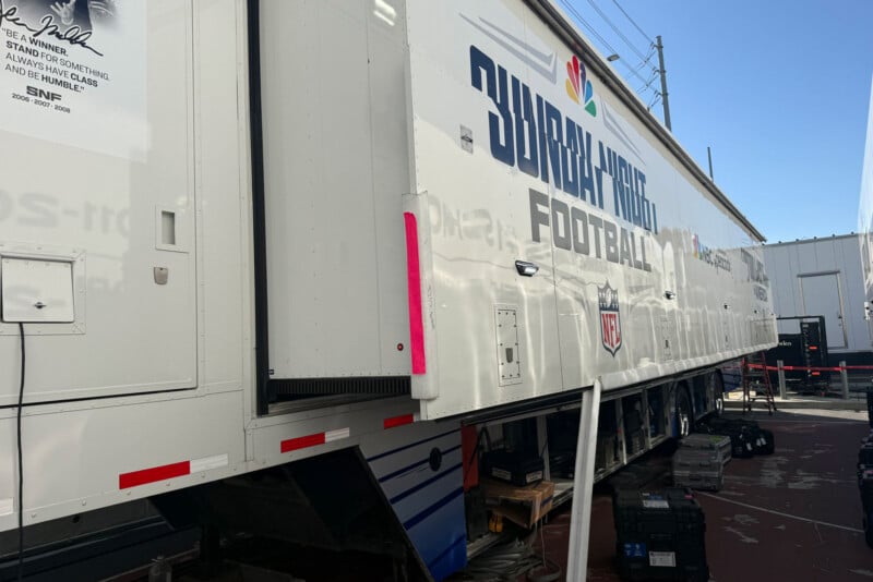 A large white trailer with the “NBC Sunday Night Football” logo and NFL shield is parked outdoors, surrounded by equipment cases and cables, with other trailers nearby.