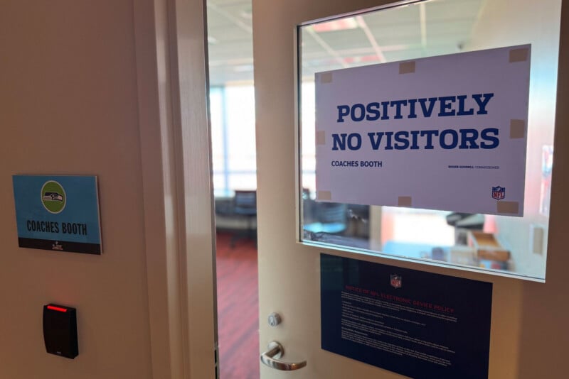 A door with a sign reading "POSITIVELY NO VISITORS COACHES BOOTH" is shown. Next to the door is a label for "COACHES BOOTH" and an NFL notice about the NFL electronic device policy.