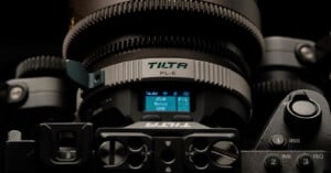 Close-up of a professional camera lens with "TILTA PL-E" branding, a digital display showing lens settings, and various camera controls in view. The image highlights intricate lens details and equipment.