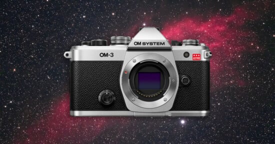 A silver and black OM System OM-3 camera is centered against a star-filled, colorful space background with a nebula visible on the right side.