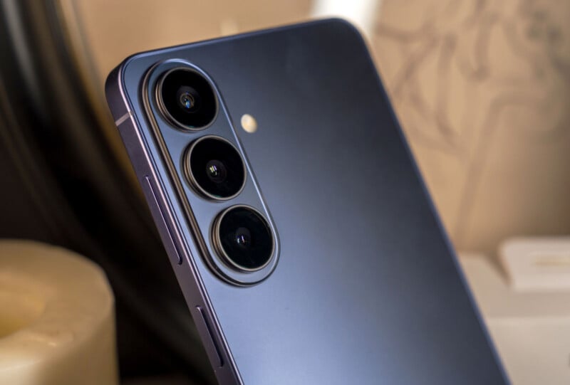 Close-up of the back of a modern smartphone with three camera lenses and a flash, featuring a sleek, metallic finish. The phone is partially folded, indicating it is a foldable device.