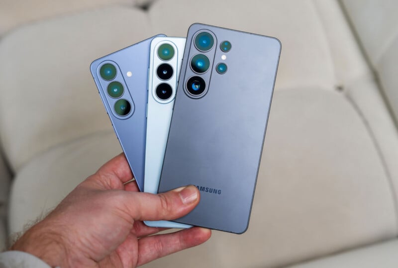 A hand holding three Samsung smartphones in different colors, all showing the back side with multiple camera lenses, against a light, blurred background.