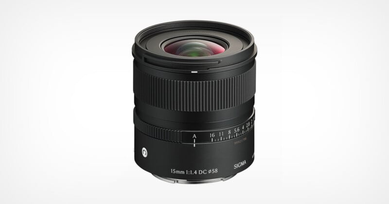 A black Sigma 15mm f/1.4 DC DN camera lens shown against a white background, with visible focus and aperture rings, lens markings, and a prominent front glass element.