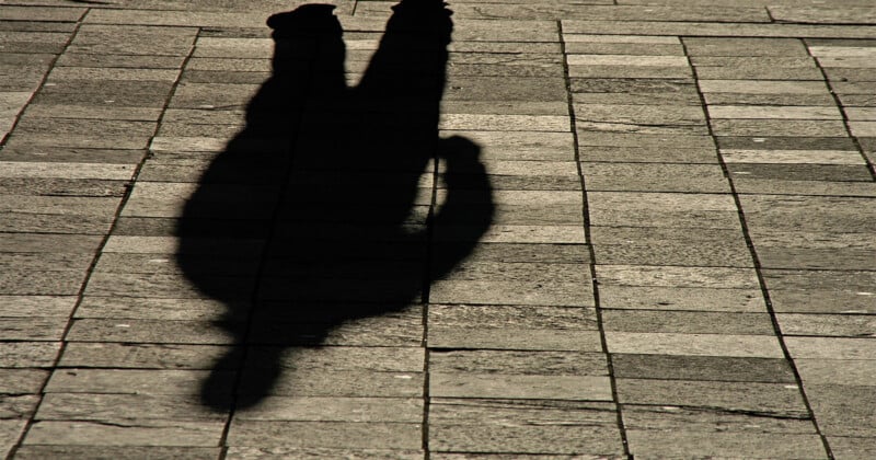 A clear shadow of a person standing on a stone-tiled pavement, with sunlight casting the silhouette sharply onto the ground.