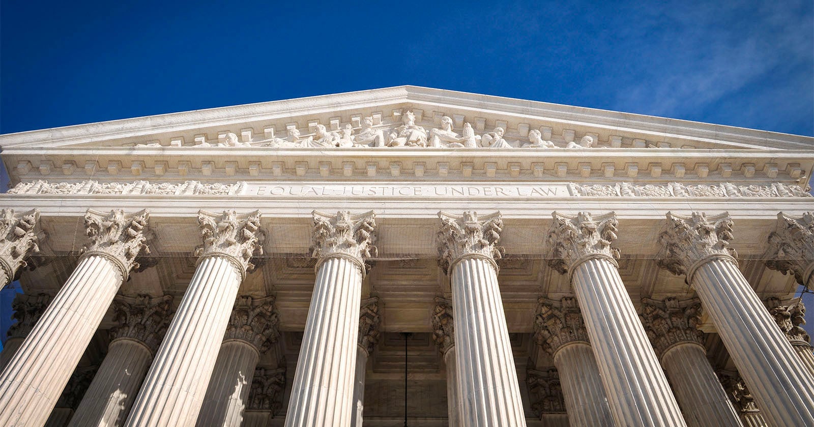 The image shows the front facade of the United States Supreme Court building, featuring tall marble columns and the inscription "EQUAL JUSTICE UNDER LAW" beneath a sculpted pediment, set against a clear blue sky.