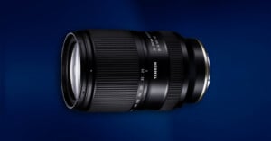 A Tamron camera lens with zoom and focus rings, shown against a dark blue gradient background.