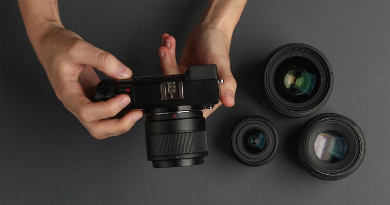 Una persona sostiene una cámara digital con una lente colocada, mientras tres lentes de cámara adicionales están alineadas sobre una superficie oscura cercana.