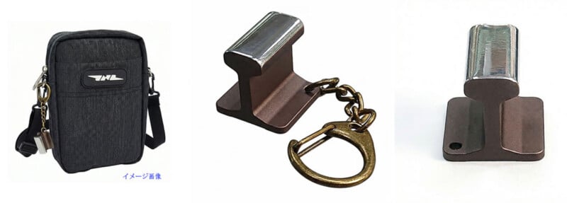 A compact black shoulder bag with a logo, shown alongside a metallic keychain shaped like a small railroad rail, attached to a brass key ring.