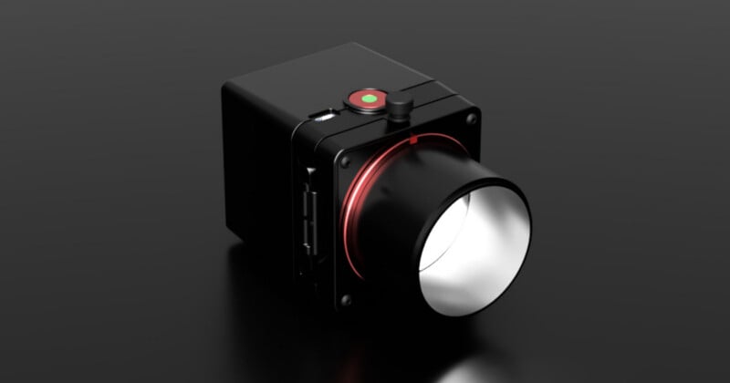 A black, box-shaped camera with a large lens and a red ring around its base sits on a reflective dark surface. The camera has a round green and red button on top and several ports on the side.