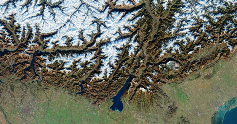La vista satelital muestra Alpes cubiertos de nieve con valles profundos, un prominente lago azul oscuro (Lago de Ginebra) cerca del centro y llanuras verdes al sureste, lo que indica un terreno más bajo.