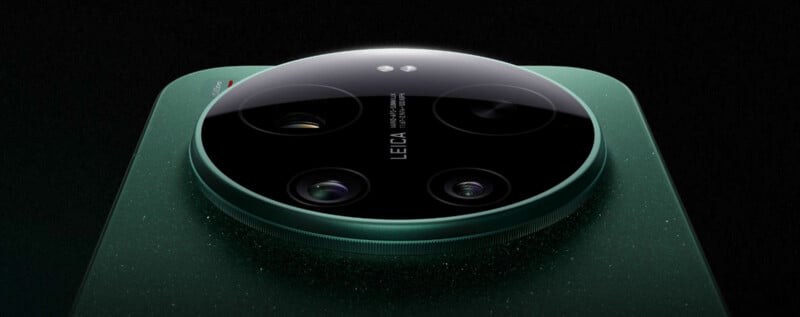 Close-up view of a green smartphone’s camera module, featuring four lenses and the Leica logo in the center, set against a dark background. The camera unit is glossy and prominently raised from the phone’s surface.