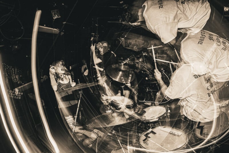 A high-energy, sepia-toned photo of a live punk band performance, with a vocalist passionately singing and musicians playing drums and guitar. Light trails and motion blur emphasize the chaotic atmosphere.