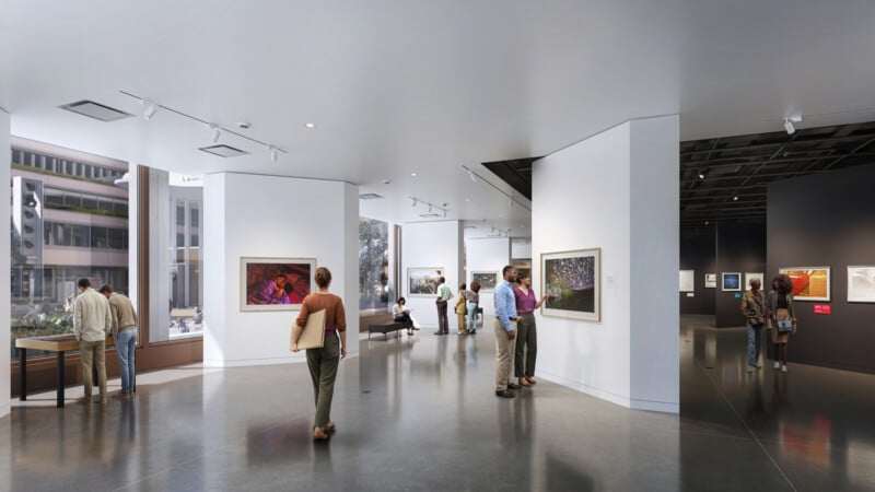 People view artwork in a bright, modern art gallery with large windows, white walls, paintings, and sculptures. Some visitors stand and observe, while others converse or sit on benches.