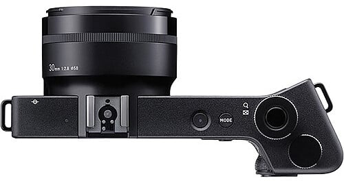 Top view of a black digital camera with a 30mm lens attached. The camera body features a mode button, power button, control dial, and hot shoe mount, all set against a white background.