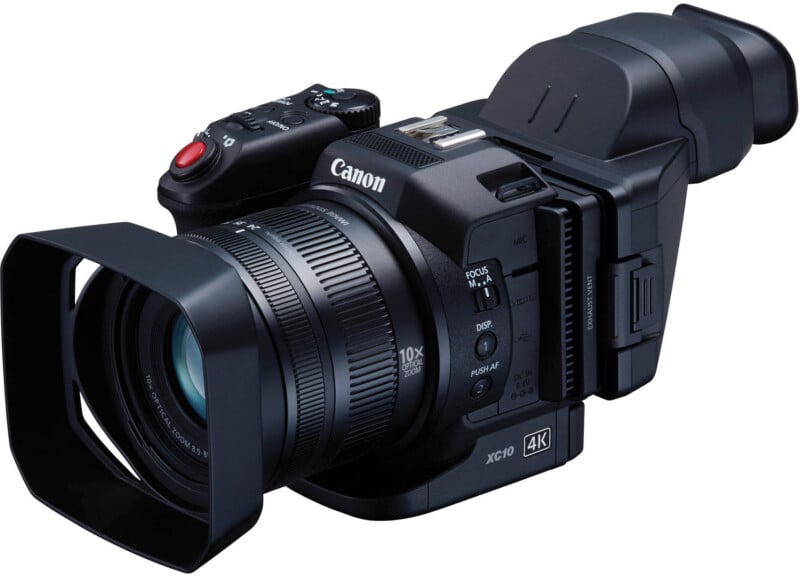 A black Canon 4K video camera with a large lens hood, viewfinder, and various buttons and dials, angled slightly to the right against a white background.