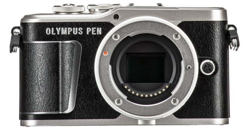 Front view of a black and silver Olympus PEN digital camera body, showing the lens mount without a lens attached and various control dials on the top.