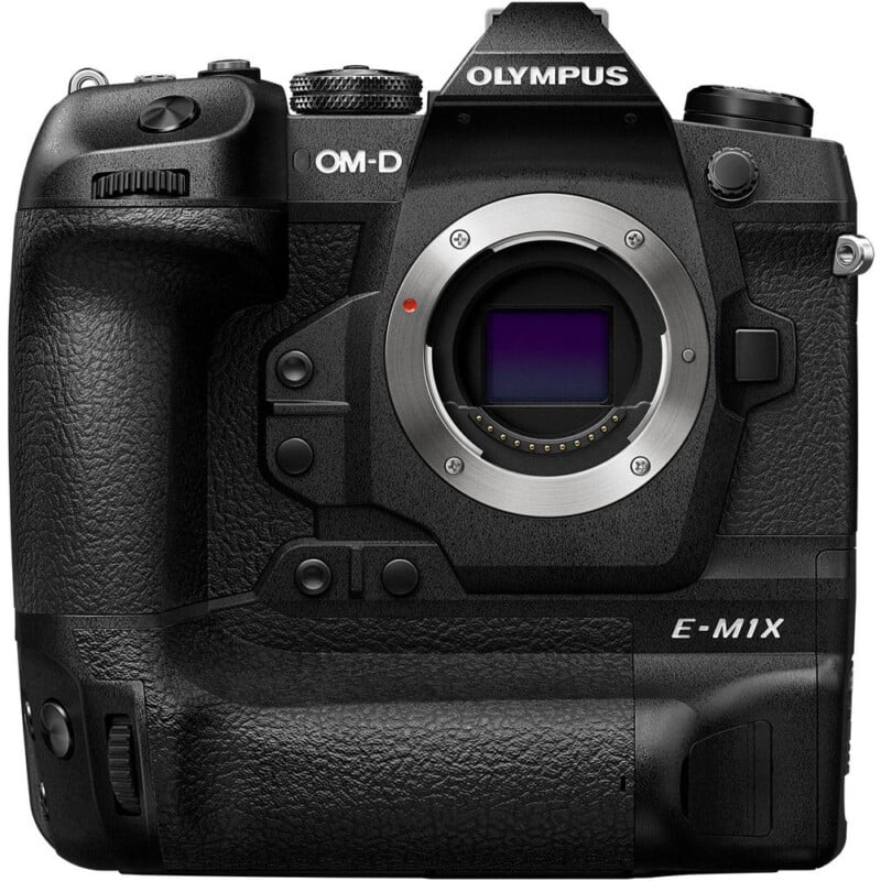 Front view of a black Olympus OM-D E-M1X digital camera body, showing the lens mount, buttons, dials, and grip. No lens is attached.