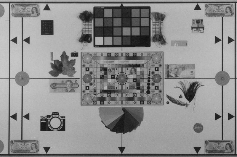 A black and white test image displays various objects arranged symmetrically on a grid, including Canadian bills, leaves, feathers, cameras, thread, a color chart, and geometric shapes.