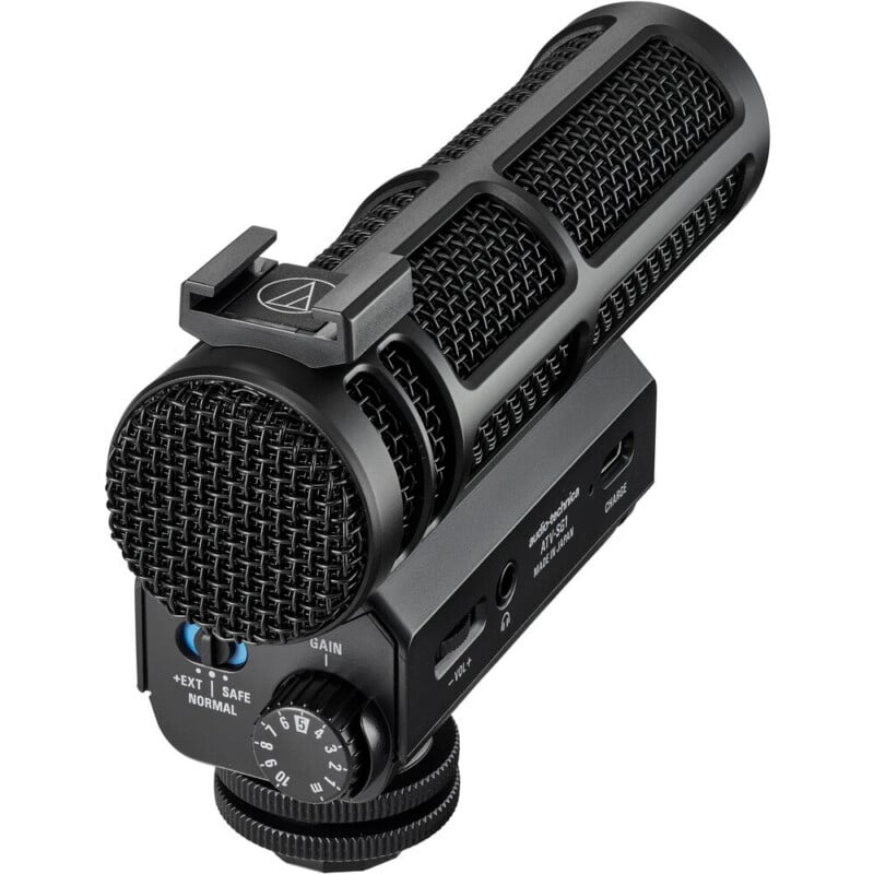 Primer plano de un micrófono negro Audio-Technica montado en cámara con rejilla de malla visible, perillas de control, interruptores y zapata para conexión de cámara.