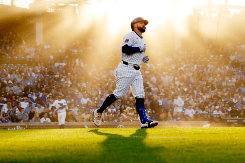 A baseball player in a striped uniform runs on the field as sunlight streams dramatically through the stadium, illuminating the crowd and casting a warm glow over the scene.