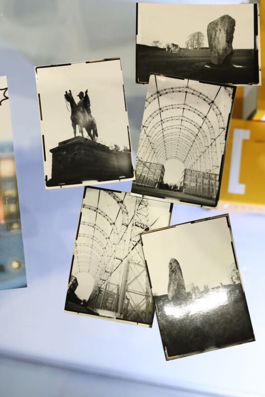 Five black-and-white photographs are laid out on a surface. Images include statues, large standing stones, and a metal arch structure, all depicting outdoor scenes and architectural or historical landmarks.