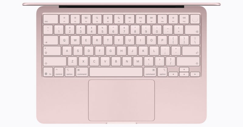 A rose gold laptop viewed from above, showing the full QWERTY keyboard and large trackpad, with black symbols on the keys.