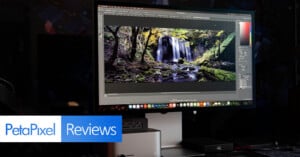 A desktop monitor displays a photo editing software with an image of a forest waterfall. The scene is dark, and the PetaPixel Reviews logo appears in the lower left corner.