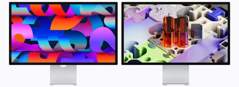 Two computer monitors with silver stands display colorful abstract digital art; the left shows bold geometric shapes in blue, pink, and orange, while the right features 3D puzzle pieces and translucent objects in pastel shades.