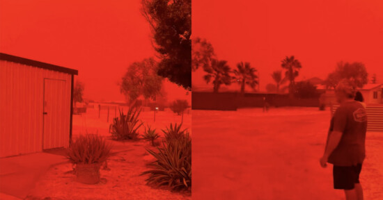 A landscape is bathed in an intense red-orange hue, with buildings, trees, and a person walking outside. The sky appears completely red, likely due to a dust storm or severe atmospheric conditions.