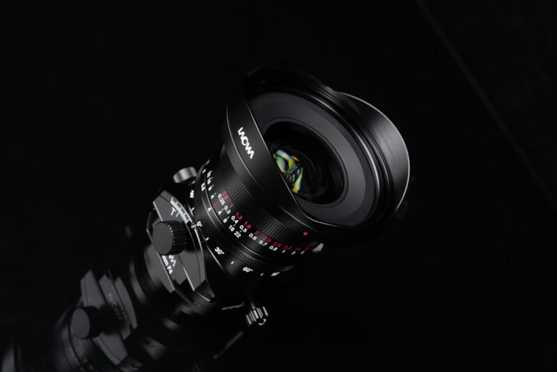 A close-up of a black Laowa camera lens with aperture and focus markings, set against a dark background.