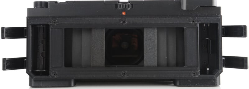 A close-up view of an open film camera back, showing the film chamber, pressure plate, and film guides with the camera's interior components visible.