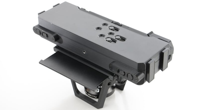 A black, rectangular camera mounting plate with multiple screw holes, side latches, and a base bracket, designed for securely attaching camera equipment to tripods or stabilization systems.