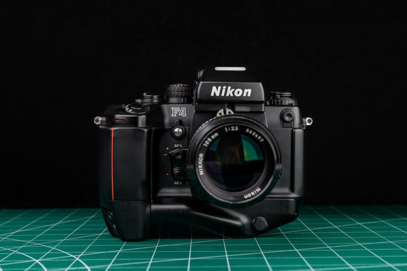 A Nikon F4 film camera with a lens attached is placed on a green cutting mat against a solid black background.