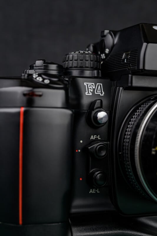 Close-up of a black Nikon F4 film camera showing its controls, including the AF-L and AE-L buttons, dials, and part of the lens mount, against a dark background.