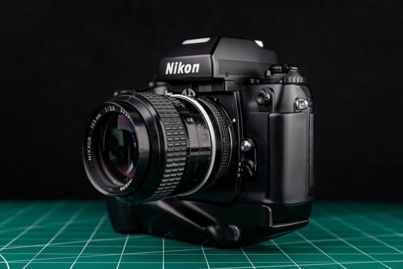 A black Nikon film camera with a large lens is placed on a green cutting mat, shown against a dark background.