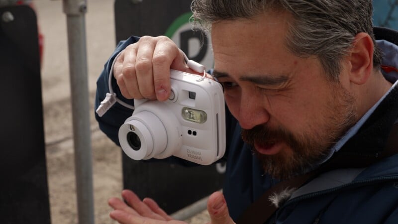 Un hombre de cabello gris y barba se acercó una cámara Polaroid blanca a la cara, preparándose para tomar una fotografía. Entrecerró un ojo y se concentró en enfocar.