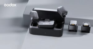 A Godox wireless microphone set is displayed on a gray surface, including a charging case, two microphones, and two receivers, with the Godox logo visible in the top left corner.