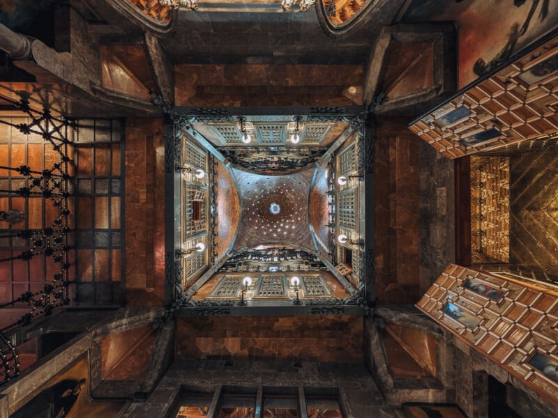 Ornate ceiling view of an elaborate, square-shaped interior dome with intricate patterns, colorful mosaics, chandeliers, archways, and detailed architectural designs in a grand historic building.