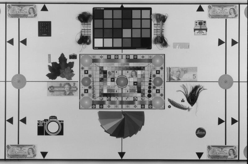 A flat lay of various objects on a white surface, including Canadian bills, maple leaves, a feather, a game board, a color chart, toy cameras, string, and geometric patterns arranged symmetrically.