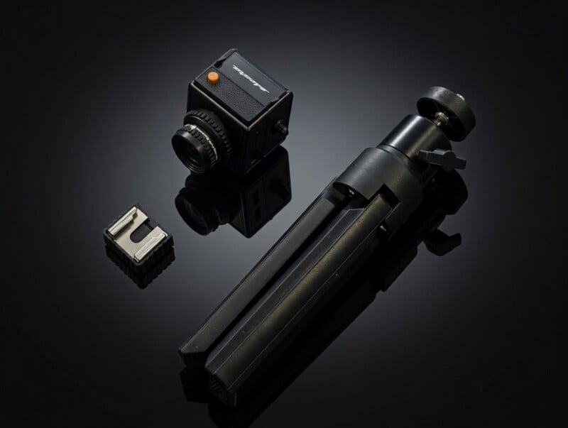 Una cámara negra compacta, un pequeño accesorio de cámara de metal y un trípode negro plegable están dispuestos sobre una superficie negra reflectante.